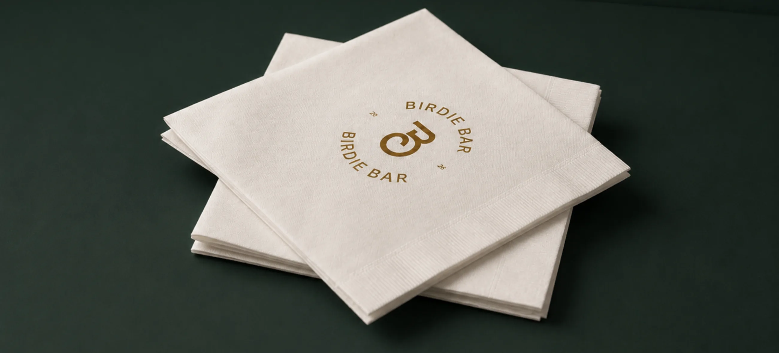 A stack of cream napkins with the gold Birdie Bar seal