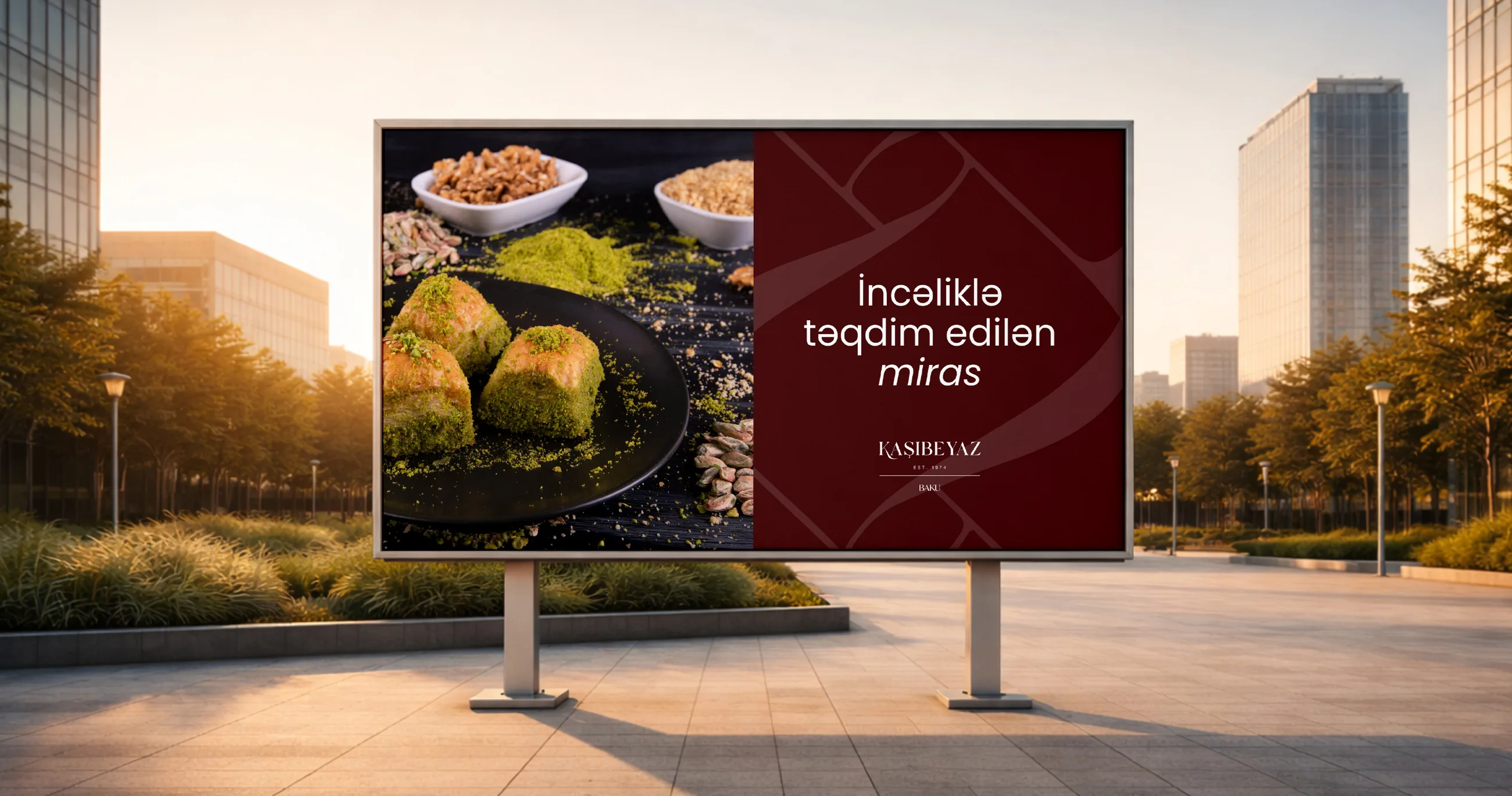 A Kaşıbeyaz billboard in a park with baklava and the line İncəliklə təqdim edilən miras